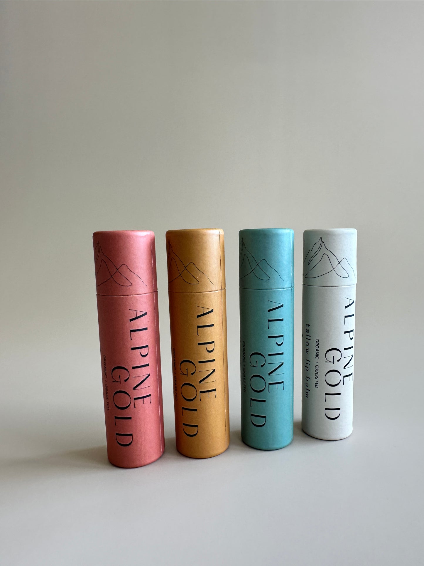 Four cardboard lip balm tubes in a variety of colors on a neutral background all containing organic tallow lip balm