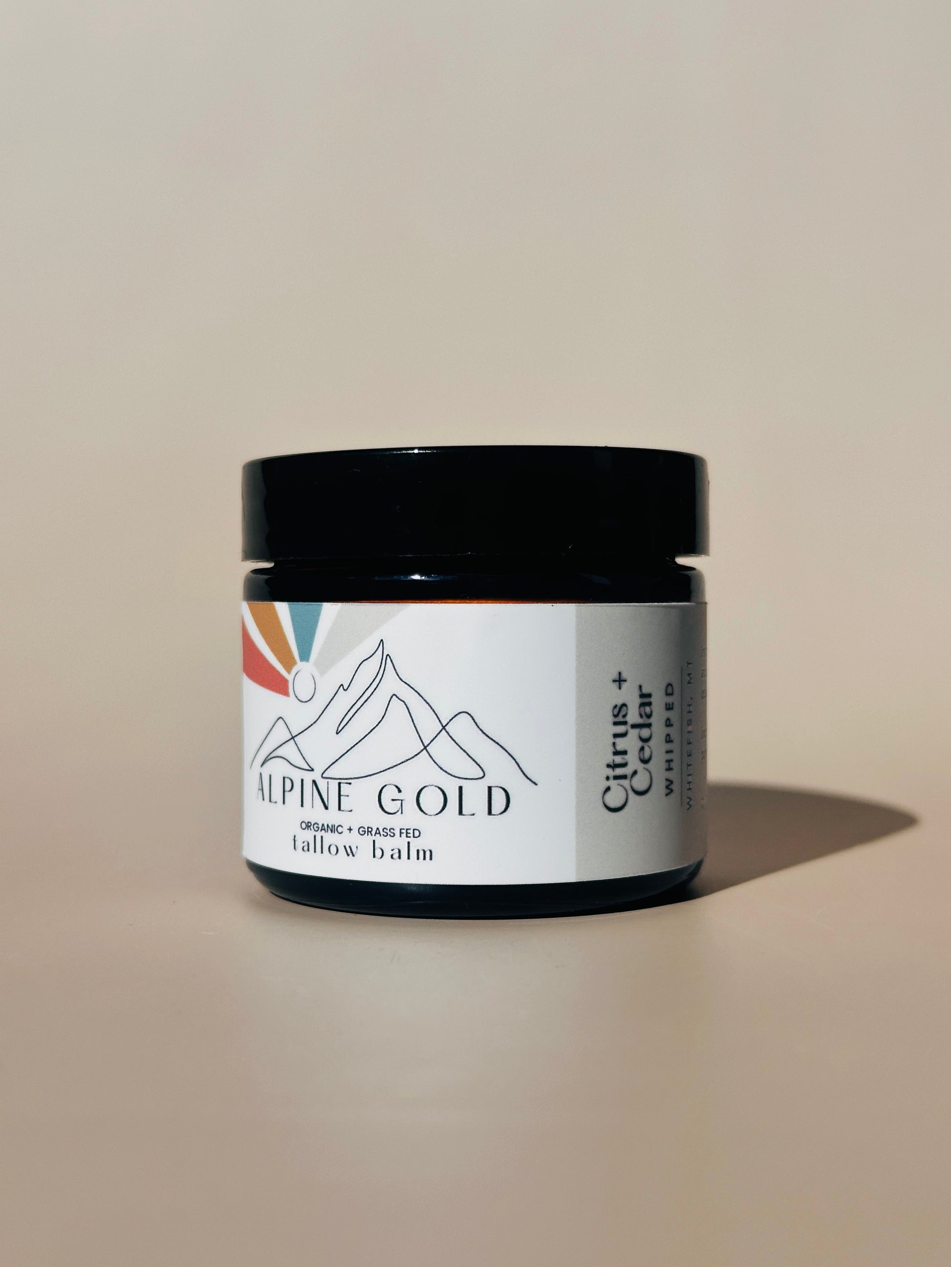 Jar labeled 'Alpine Gold' on a neutral background - citrus and cedar organic tallow balm