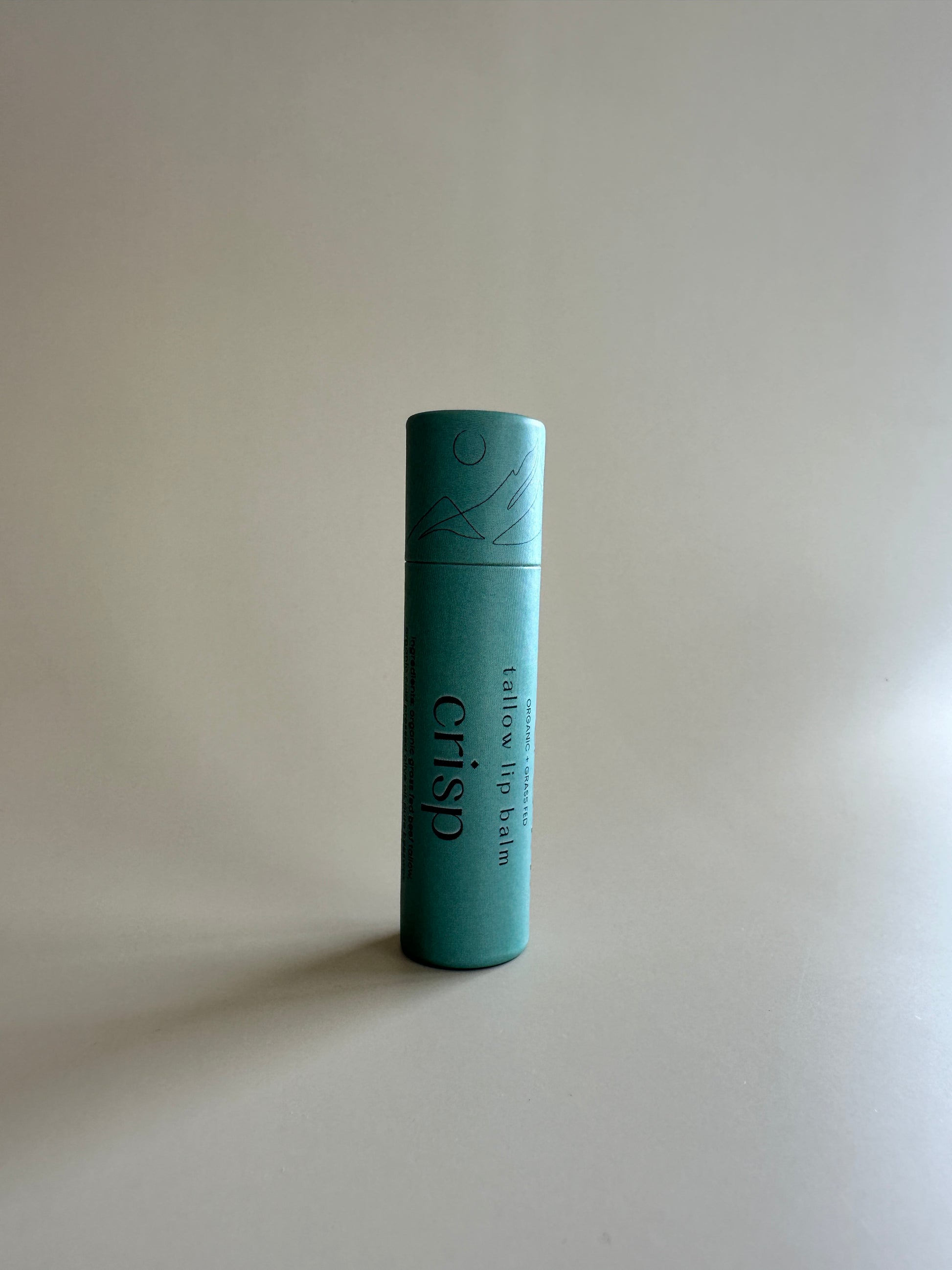 Cardboard tube containing organic tallow lip balm in spearmint, basil, and orange on a neutral background.