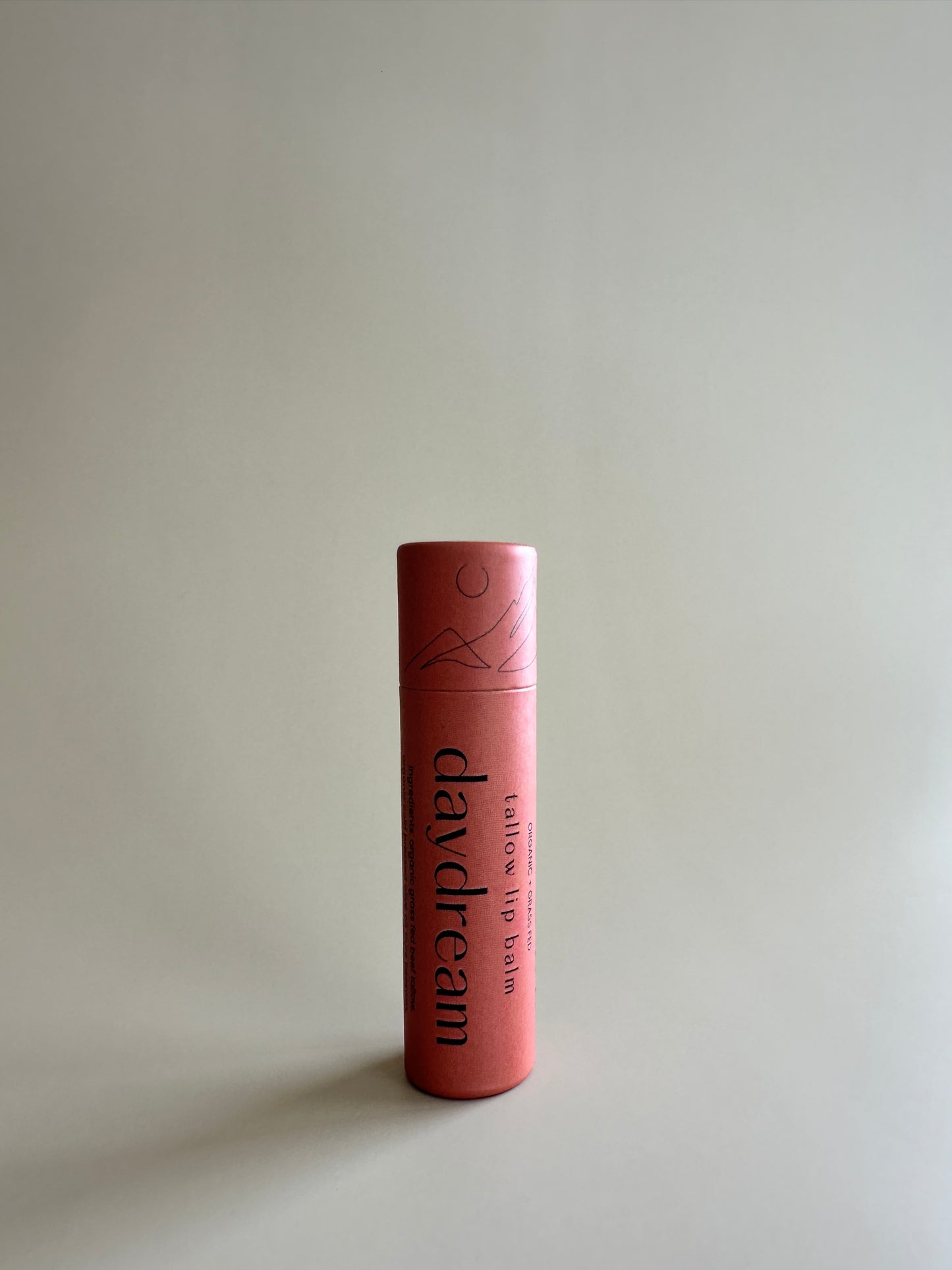 Cardboard tube containing organic tallow lip balm in chamomile on a neutral background.