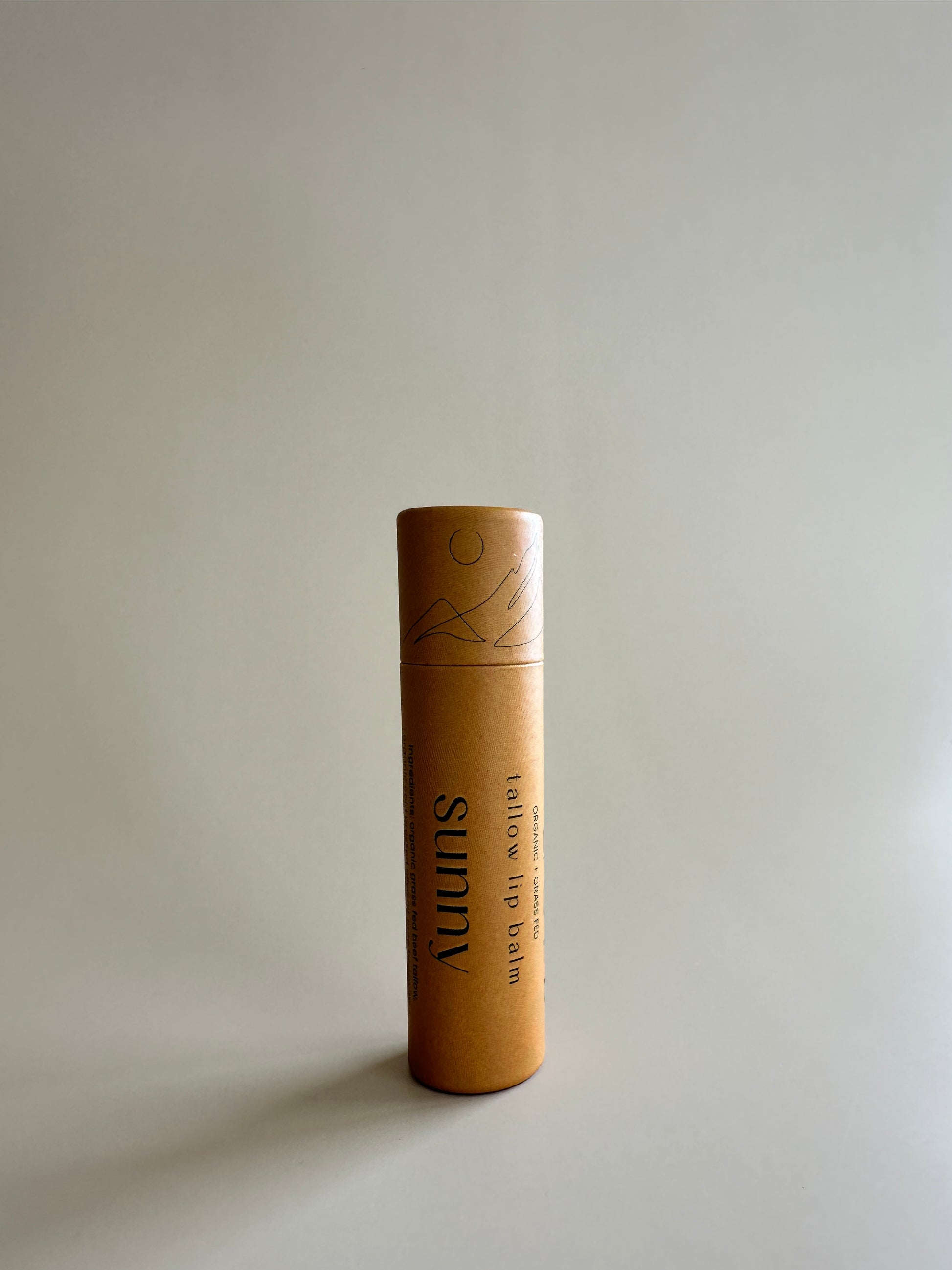 A cardboard tube of lip balm with a natural beige color, placed against a neutral background.