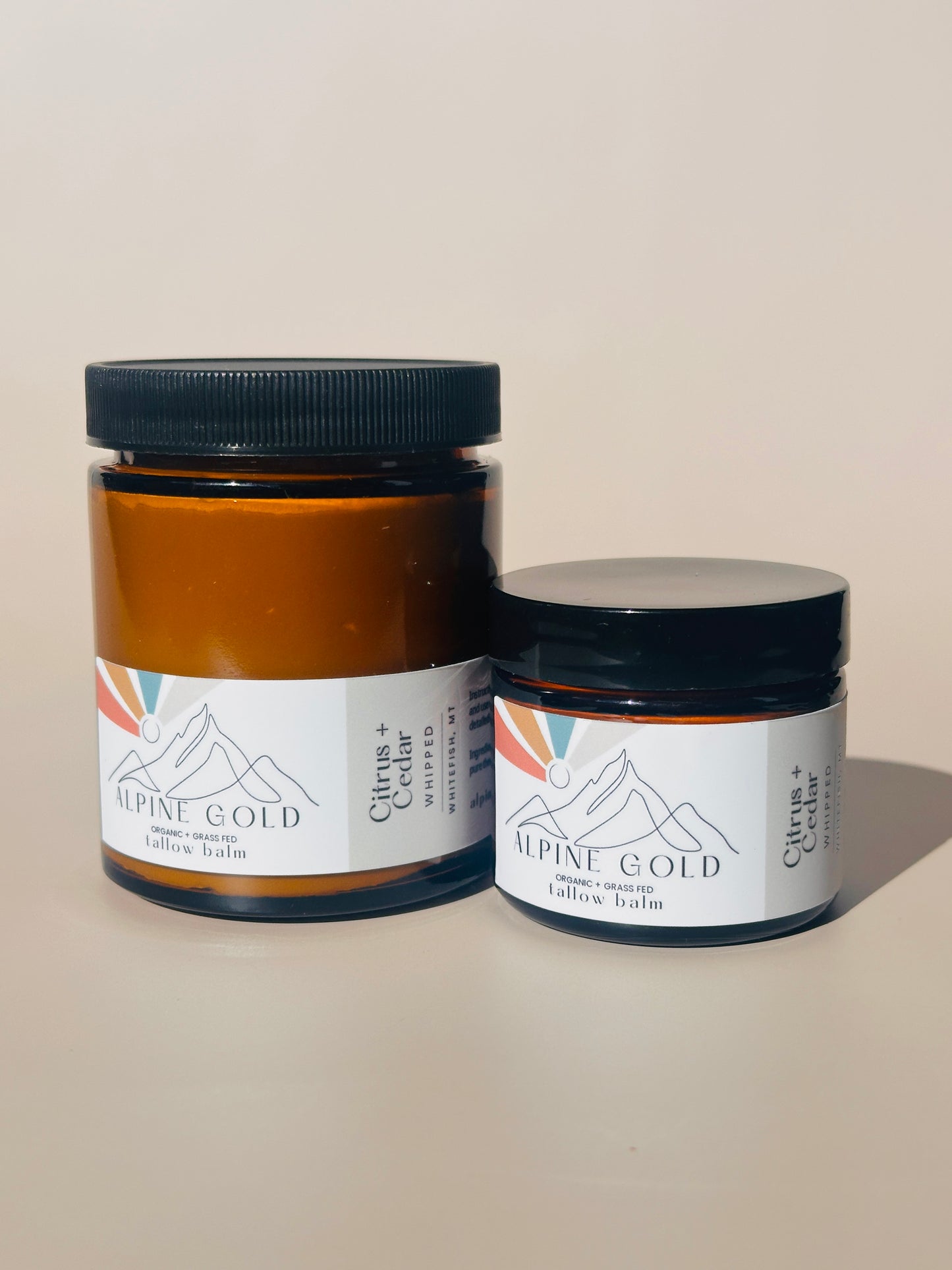 Two jars labeled 'Alpine Gold' on a plain background organic tallow balm grass fed