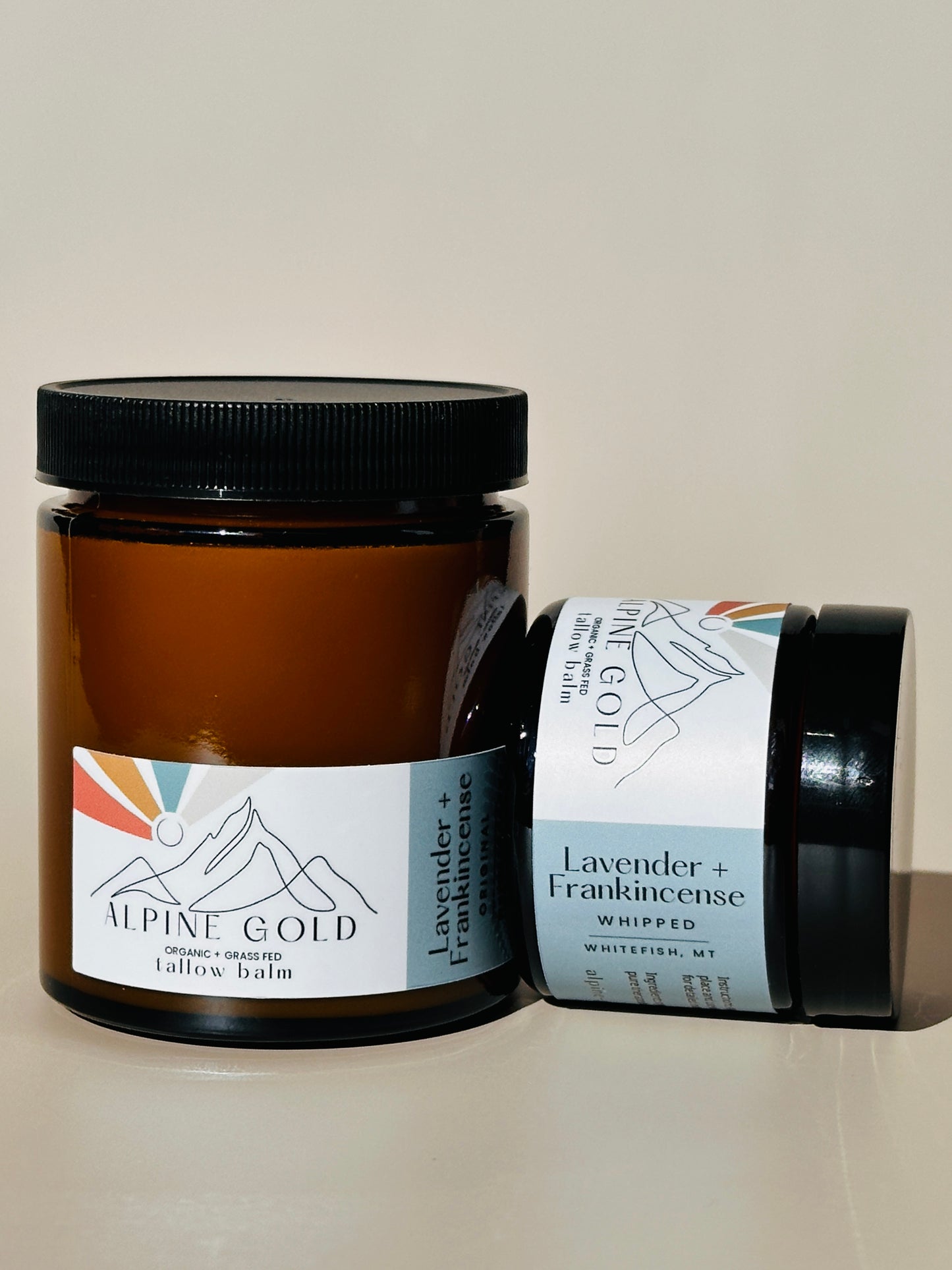 Two jars of tallow balm with labels on a neutral background